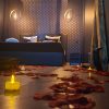 ue basse de la Love Room L'Aixtase avec pétales de roses et bougies sur le sol, menant à un lit élégant dans une ambiance intimiste éclairée par des lampes suspendues modernes