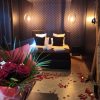 Bouquet de roses rouges en premier plan avec une chambre romantique en arrière-plan, lit noir capitonné entouré de pétales et de bougies, créant une atmosphère intime.